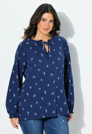 Blouse à manches longues bleu marine avec un col à volants, un détail à nouer et un imprimé d'oiseaux bleu clair. Textile doux, coupe décontractée et poignets élastiques.