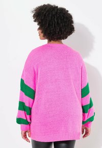 Oversized sweater in het roze met groen en roze gestreepte mouwen. Gebreide textuur met ribgebreide manchetten en zoom. Relaxte pasvorm, ronde halslijn.