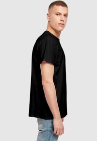 Black cotton t-shirt with short sleeves, crew neckline, smooth texture, displayed on a male model turned slightly to the side.