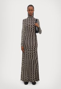 Robe longue à motifs zigzag noir et blanc avec un col montant et des manches longues, accompagnée d'un petit sac noir et de chaussures noires.