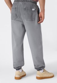 Grijze sweatpants met een zachte textuur, elastische tailleband en zichtbare achterzakken. Gemaakt in combinatie met beige sneakers met lichte zolen.
