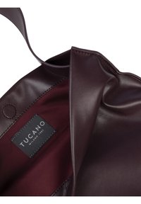 Maroon leather tote bag with a smooth texture, featuring a branded interior tag. The interior is a deep burgundy fabric.