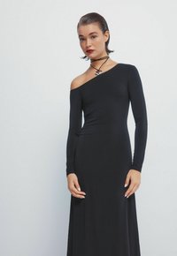 Zwarte, aansluitende jurk met één schoudervrij mouw, lange mouwen en een gladde, lichte textuur. Inclusief een hartvormige choker.