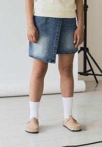 Falda de denim con un degradado de claro a oscuro, corte asimétrico y dobladillo sin acabar. Combinada con calcetines blancos y zapatos de tela beige.