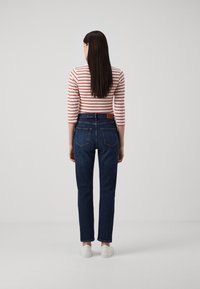 Stripete langermet topp og mørkeblå jeans med baklommer, rett ben design, og en brun lærpatch. Brukt med hvite sneakers.