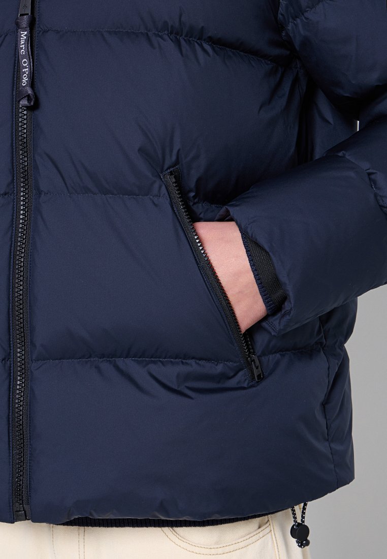 Marineblaue Daunenjacke mit einem Reißverschlussfach, gestepptem Design und elastischen Bündchen für eine taillierte Passform. Das Material wirkt leicht und isoliert.