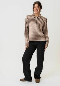 Smeđi i krem prugasti dugi rukav polo majica s gumbima, u kombinaciji s crnim širokim hlačama i smešnim mokasinkama.