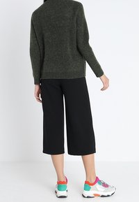 Grüner gestrickter Pullover, schwarze weite cropped Hose und mehrfarbige Sportschuhe mit weißem Grund und bunten Akzenten.