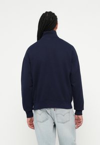 Marineblauwe sweatshirt met een hoge kraag, dropped shoulders en geribbelde manchetten. Opvallende zachte textuur, iets cropped pasvorm bij de taille.