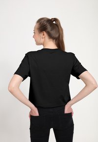 Černé tričko s krátkým rukávem a kulatým výstřihem, vyrobené z bavlny. Zadní pohled ukazuje uvolněný střih a hladkou texturu na neutrálním pozadí.