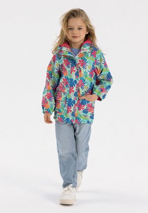 Veste colorée à motifs floraux avec fermeture éclair sur le devant et poches, associée à un jean bleu clair et des baskets blanches.