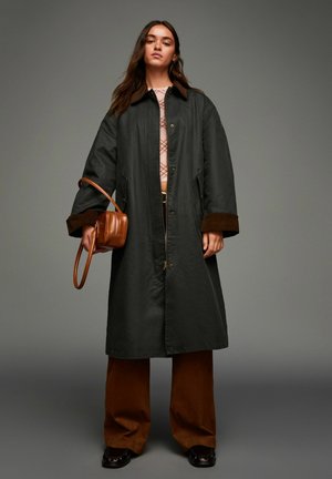 Black outerwear coat with brown suede accents, featuring a button front, large pockets, and relaxed fit, paired with brown wide-leg pants.