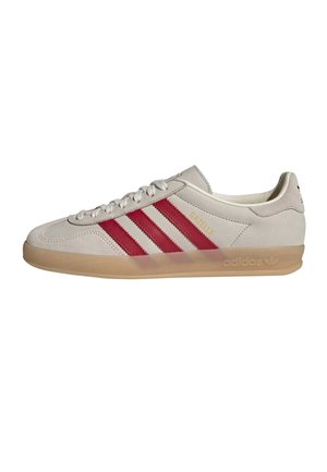 Biały sneaker Adidas Gazelle z czerwonymi paskami i przezroczystą gumową podeszwą, pokazany z boku na białym tle.