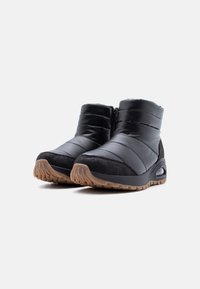 Ζευγάρι μαύρα επενδεδυμένα μποτάκια αστραγάλου με καφέ υφασμένους πάτους και πλαϊνά κλεισίματα με φερμουάρ, σχεδιασμένα για κρύο καιρό.