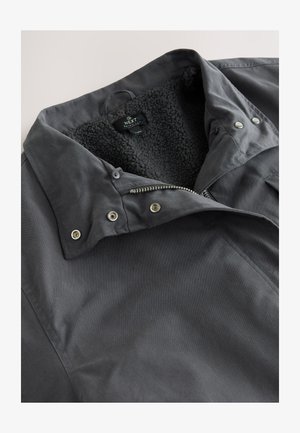 Szürke szövetkabát puha, fekete, szőrmebéléssel ellátott gallérral, patentos gombokkal és elöl cipzárral. Sima textúrájú és hétköznapi kialakítású.