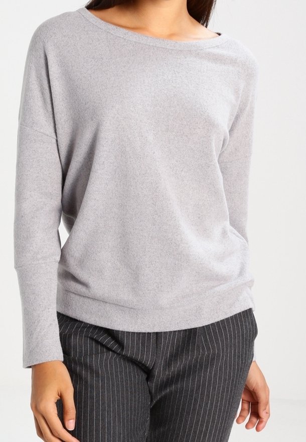 Jasnoszara bluzka z długim rękawem o szerokim dekolcie i luźnym kroju, wykonana z miękkiego materiału. Połączona z czarnymi spodniami w cienkie paski.