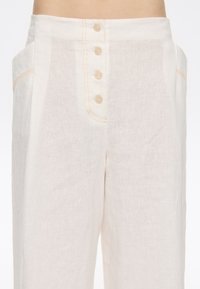 Linen trousers in light cream, featuring a four-button closure with a subtle orange stitch detail and side pockets. Smooth texture.