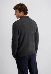 Dunkelgrauer Strickpullover mit geripptem Kragen und Saum. Einfaches Design mit langen Ärmeln und lockerer Passform, kombiniert mit marineblauen Hosen.
