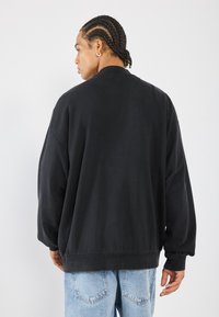 Black oversized sweatshirt with a round neckline and ribbed cuffs. Fabric appears soft with a smooth texture. Worn with light blue jeans.