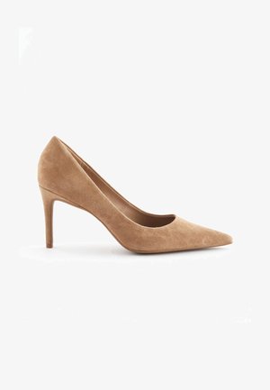 Chaussure à talon haut en daim beige avec un design à bout pointu et un talon fin. La texture est lisse avec une finition douce. Aucun matériel ou accent visible.