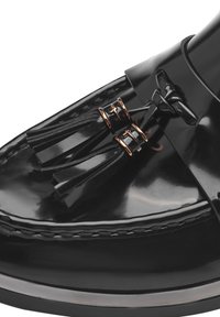 Svarte lakkloafere med en jevn, blank tekstur, prydet med svarte dusk og metalliske gulldetaljer. Detaljert søm langs sålen.