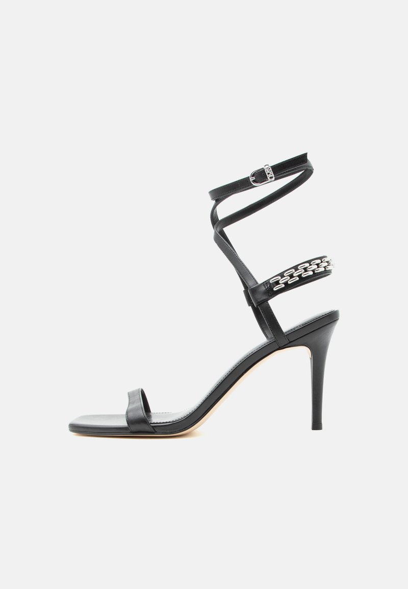 Μαύρο σανδάλι με ψηλό τακούνι, λεπτό λουράκι στον αστράγαλο, λουράκι στη μέση του ποδιού διακοσμημένο με ασημένιες αλυσίδες και ανοιχτή μύτη.