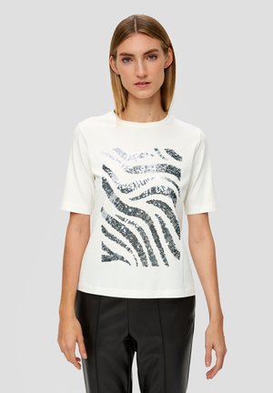 T-shirt blanc à manches courtes avec un motif ondulé en paillettes argentées et noires. Le tissu est lisse ; la coupe est décontractée et légèrement carrée.