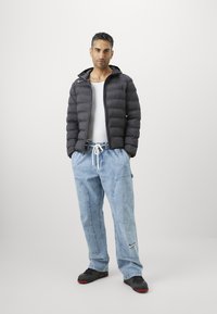 Sort puffer-jakke med quiltet mønster, hvid T-shirt, lyseblå baggy jeans med sidelommer og sorte sneakers med røde accenter.