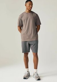 Graues Baumwoll-T-Shirt mit rundem Ausschnitt und kurzen Ärmeln, kombiniert mit dunkelgrauen Shorts und grauen Sneakers mit weißen Akzenten.