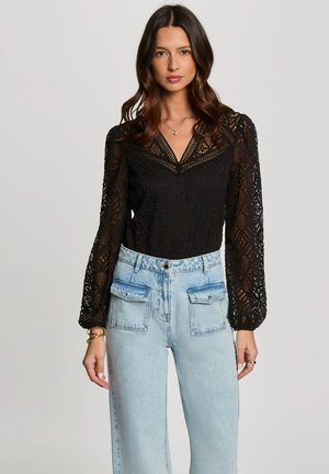 Body en dentelle noire avec de longues manches bouffantes, décolleté en V et motifs découpés complexes, associé à un jean en denim léger taille haute bleu.