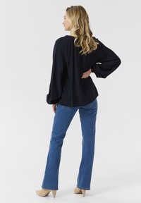 Blusa blu navy con dettaglio delle spalle arricciato, abbinata a jeans blu a zampa d'elefante e tacchi beige. Tessuto morbido, vestibilità comoda e maniche lunghe.