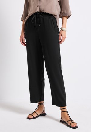 Pantaloni neri larghi con vita elasticizzata e cordino. Abbinati a sandali neri minimalisti. Tessuto morbido, taglio dritto.