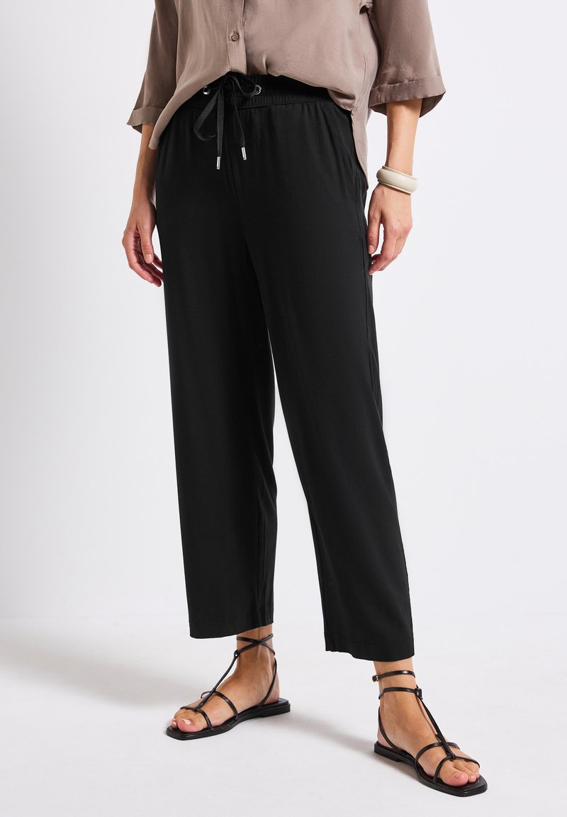 Black, loose-fitting pants with an elastic waistband and drawstring. Paired with minimalistic black sandals. Smooth fabric, straight cut.