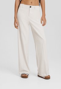 Vidbyxort i ljusbeige tyg, med knappstängning, sidofickor och en mjuk textur, stylade med platåsandaler.