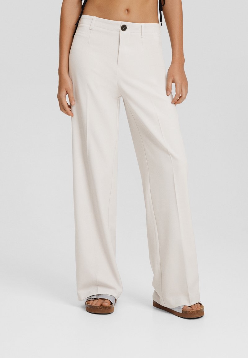 Vidbyxort i ljusbeige tyg, med knappstängning, sidofickor och en mjuk textur, stylade med platåsandaler.