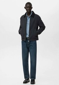 Tmavomodrá bomber bunda, svetlomodré polo tričko, modré džínsové nohavice, čierne topánky. Bunda má zipsové zapínanie a predné vrecká.