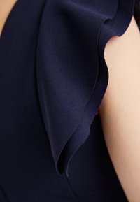 Tecido de vestido azul-marinho com uma textura suave apresenta um detalhe de ombro em camadas, destacando um movimento fluido e um drapeado elegante.