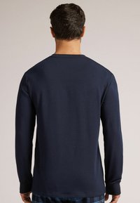 Marineblaues Langarmshirt mit Rundhalsausschnitt, geripptem Kragen und Bündchen. Glattes Material mit enganliegendem Schnitt, von hinten gesehen.