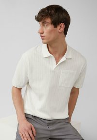 Witte polo met korte mouwen en een gemêleerd verticaal streep patroon, met een kraag en een borstzak. Gecombineerd met grijze broek.