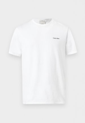 Valge lühikeste varrukatega T-särk ümara kaelusega, millel vasakul rinnal väike must "Calvin Klein" logo, kuvatud ühevärvilisel taustal.