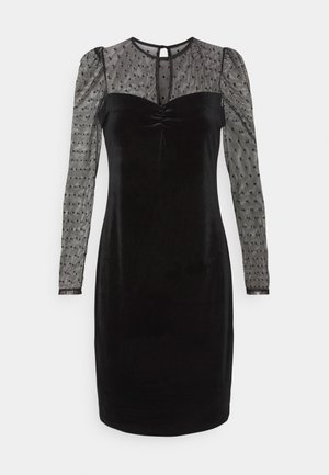 Robe en velours noir avec manches longues transparentes et empiècement à petits pois, encolure froncée et fermeture par bouton à trou à l'arrière.
