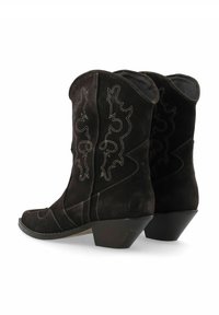 Bottes de cowboy en daim noir avec des coutures décoratives, bout pointu, talon bas et bords supérieurs incurvés. Présente une surface texturée lisse.