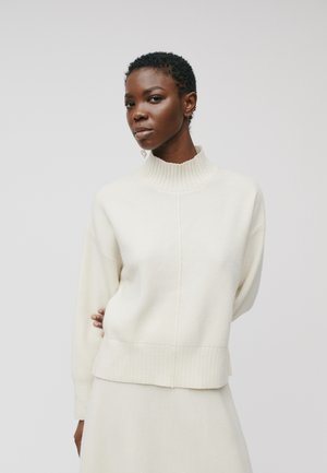 Cremefarbenes Sweatshirt mit hohem geripptem Kragen, überschnittenen Schultern und geripptem Saum. Stricktextur, kombiniert mit einem passenden Rock.