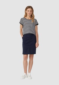Gestreepte zwart-witte top met korte mouwen gecombineerd met een marineblauwe rok tot de knieën, met twee voork vakken, aangevuld met witte sneakers.