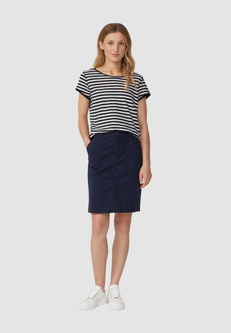Gestreepte zwart-witte top met korte mouwen gecombineerd met een marineblauwe rok tot de knieën, met twee voork vakken, aangevuld met witte sneakers.