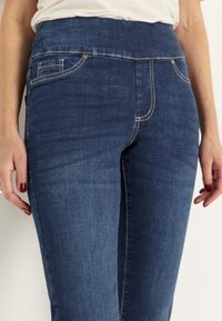 Blå denimjeans med en slät yta, med hög midja, klassisk femficksdesign och lätta sömnadsdetaljer.