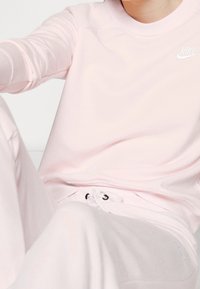 Ljusrosa Nike-tröja med långa ärmar, som har en rund halsringning och vitt logotyp. Mjukt tyg med en avslappnad passform och subtil textur.