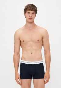 Sötétkék pamut boxeralsó, fehér elasztikus derékkal, amelyen a "Tommy Hilfiger" logó látható, és testhez simuló fazonban készült.