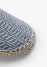 Nærbillede af blå herringbone-stof espadrille tå med beige reb-sål og tykk beige syning langs kanten.