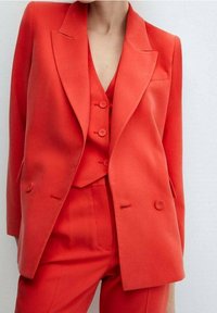 Blazer rouge ajusté à double boutonnage avec gilet et pantalon assortis, présentant une texture lisse, un col cranté et une fermeture à deux boutons.